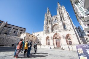 Group of visitors standing before the Gothic Burgos Cathedral under a clear blue sky in Spain.