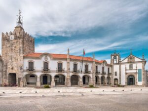 Historic town hall and church with stone tower and red‑tiled roofs in a sunny European square.