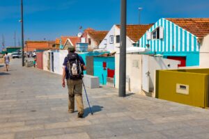 Pilgrim walking along a sunny coastal street lined with colorful striped houses in Galicia, Spain.