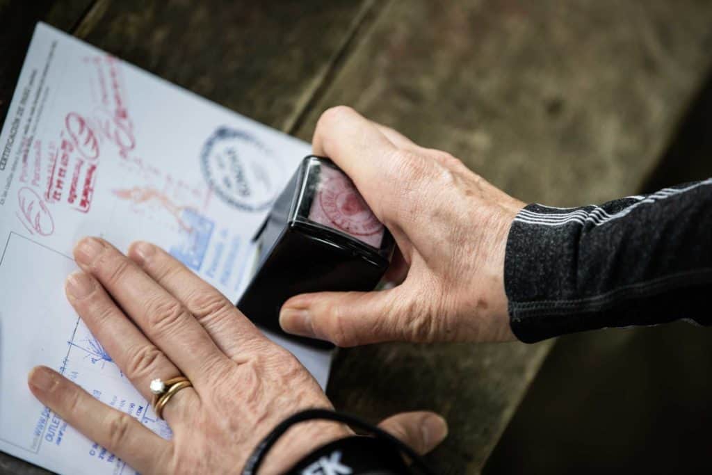 Close‑up of a pilgrim stamping a Camino de Santiago credential with an ink stamp on a wooden table.