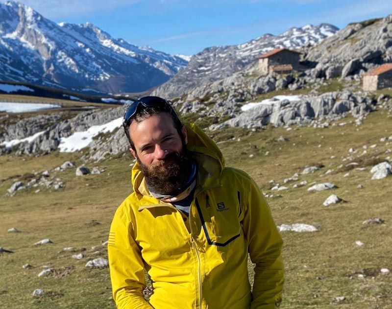 Joaquin Pereira, one of Andaspain's guides, looks at the camera wearing a yellow jacket Behind him, a stunning mountain landscape on a sunny day. 